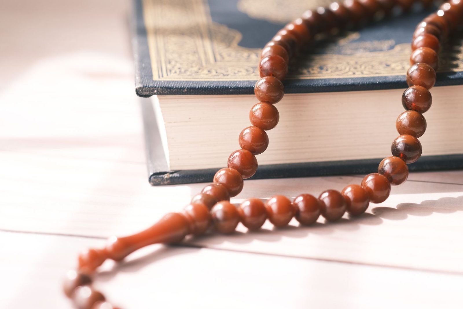 Yumuşak gün ışığında kapalı bir Kur'an-ı Kerim üzerinde duran ahşap tesbih