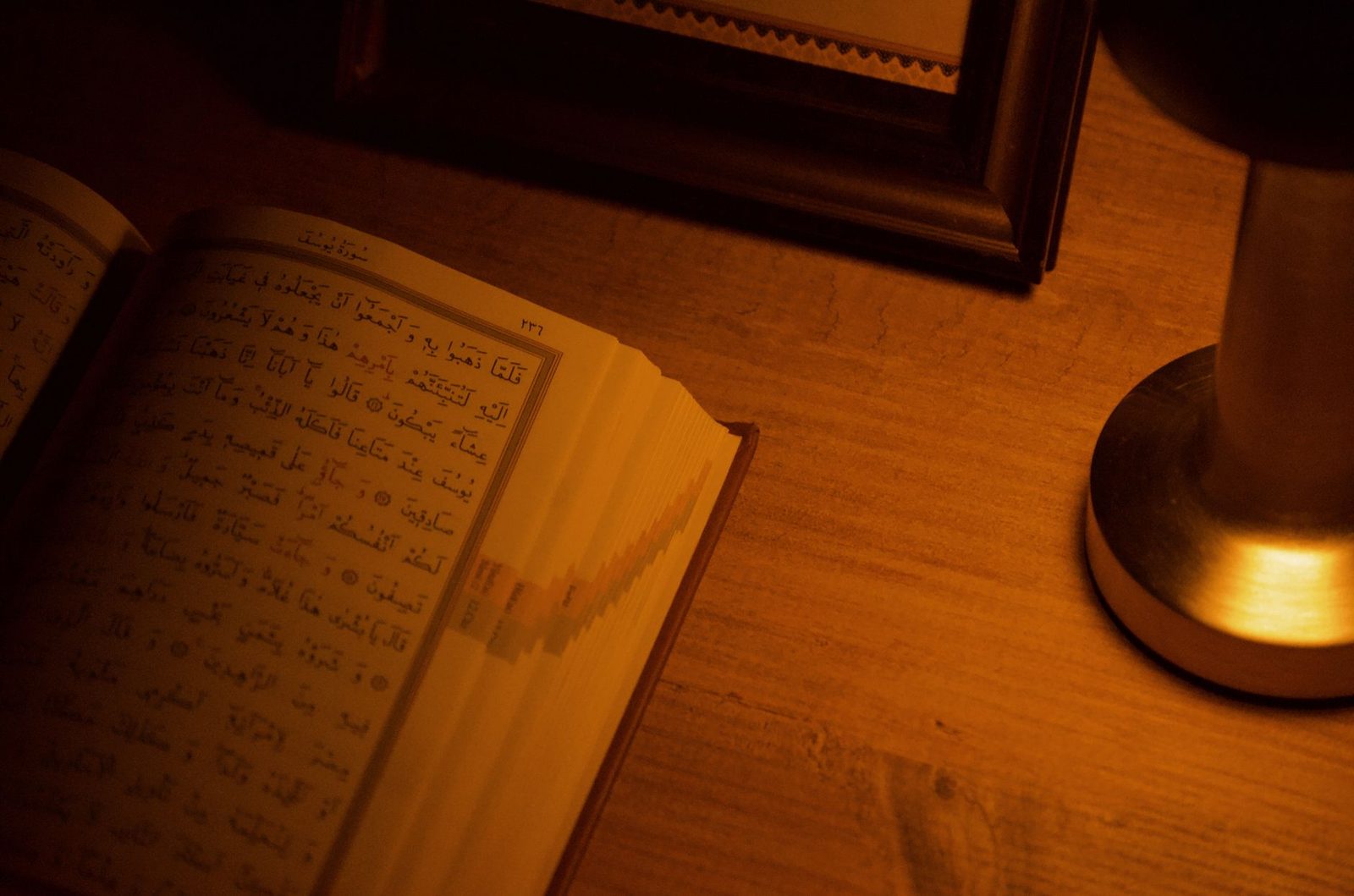 Ahşap masada açık duran Kur'an-ı Kerim ve yanan bir lamba — gece okunan Kur'an'ın temsili