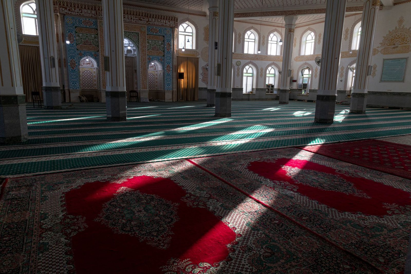 Pencerelerden süzülen güneşin kırmızı ve yeşil cami halısına düştüğü boş bir cami içi