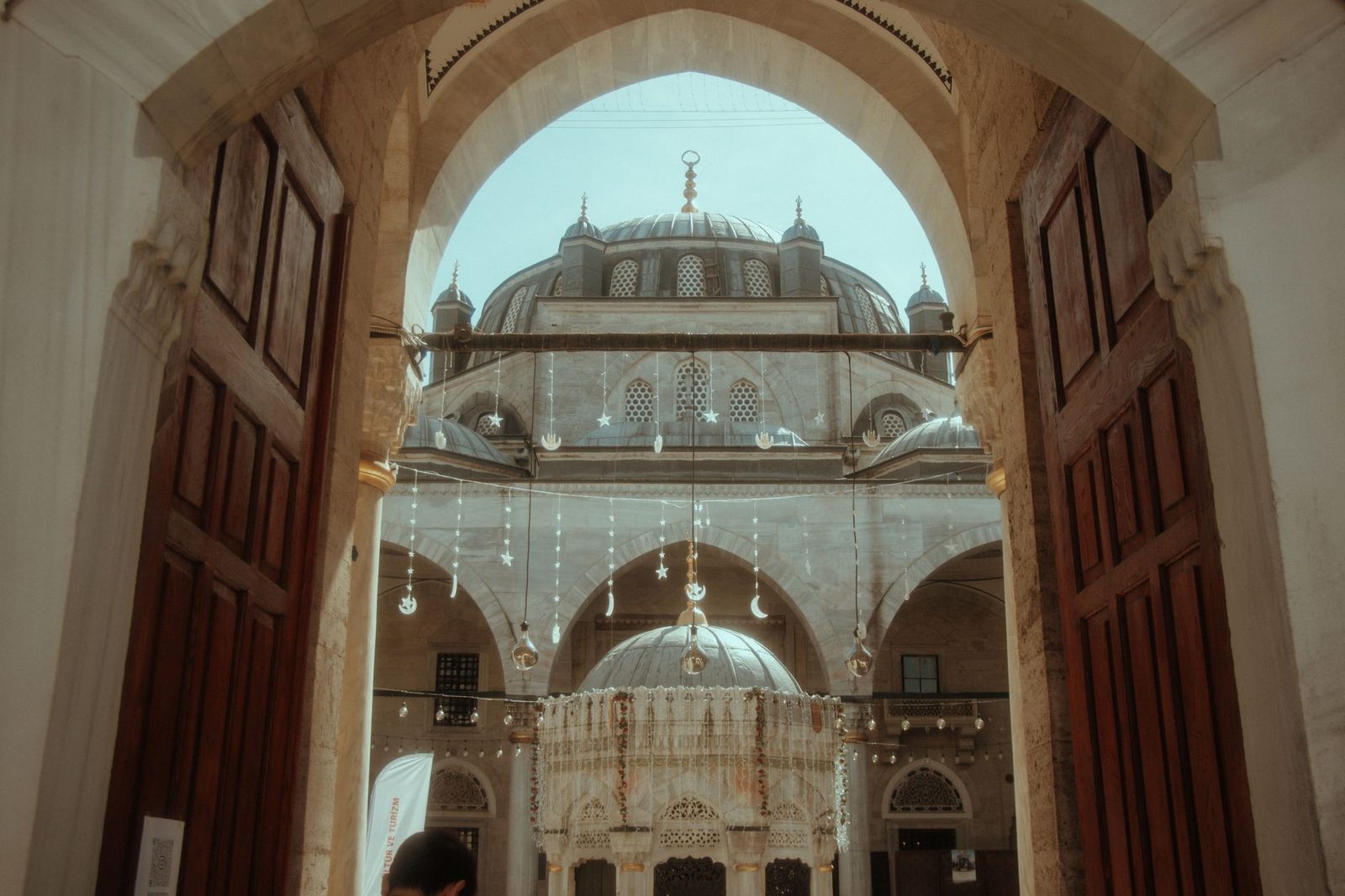Ardına kadar açık ahşap kapıların arasından görünen cami avlusu, şadırvan ve kubbeler