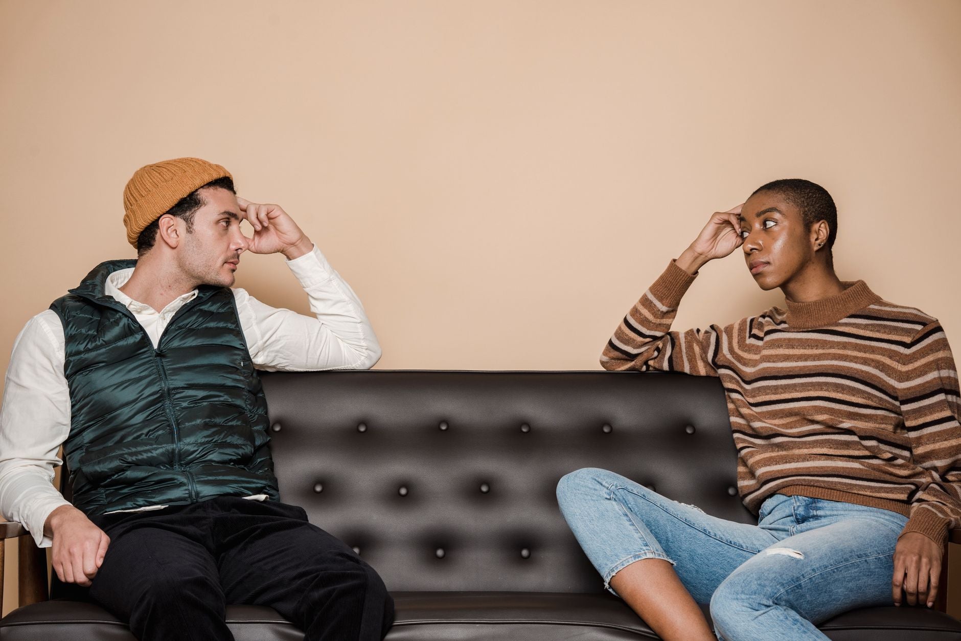 A serious-looking couple sitting on a couch in tense silence — one partner's body language closed, the other looking away