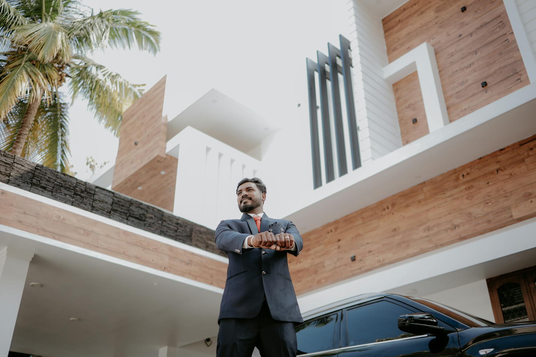 Confident man in a suit standing beside a modern home, representing pride in success and the exposure it can create
