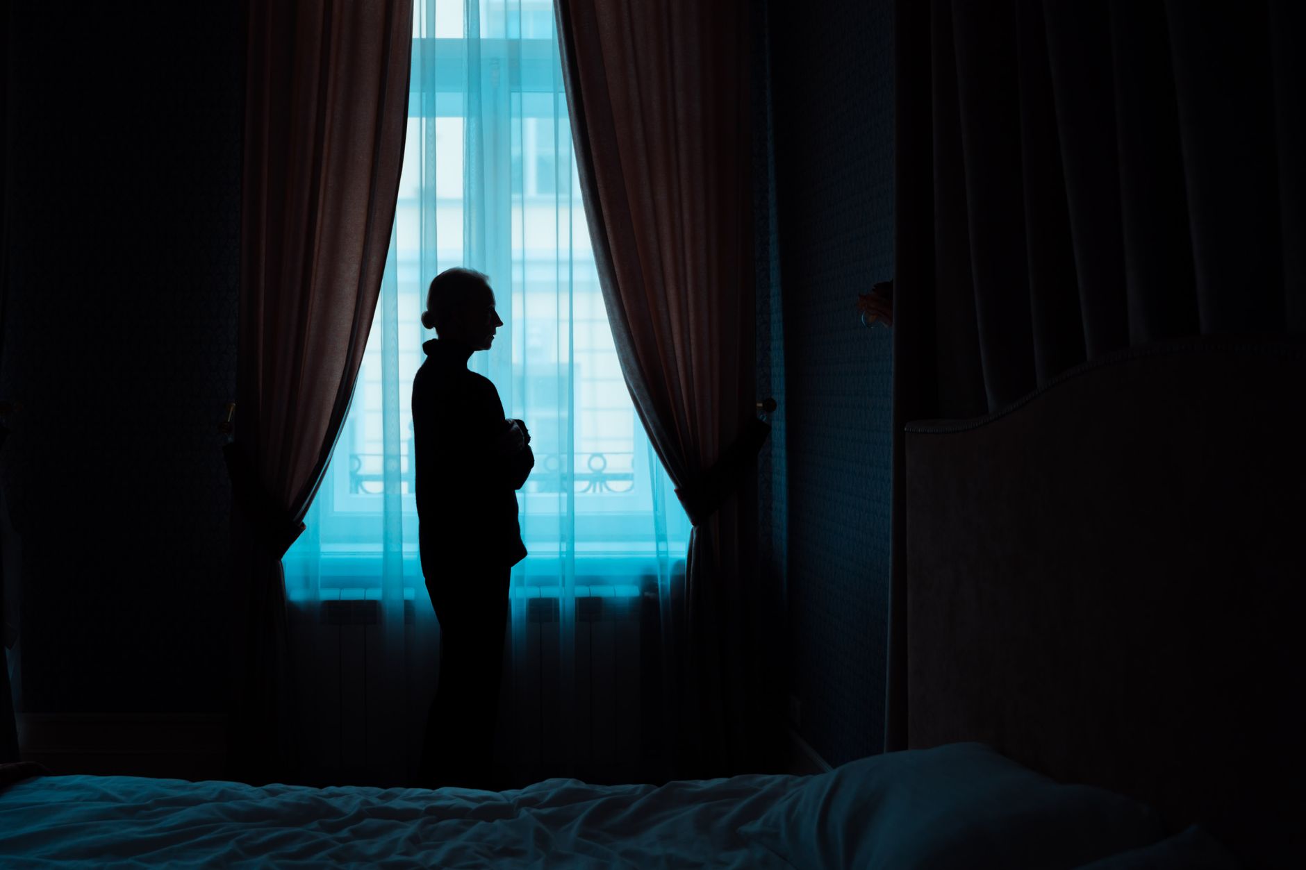 Evil Eye and Anxiety — a woman sitting alone in a softly lit room, one hand at her chest, the unease visible in her posture