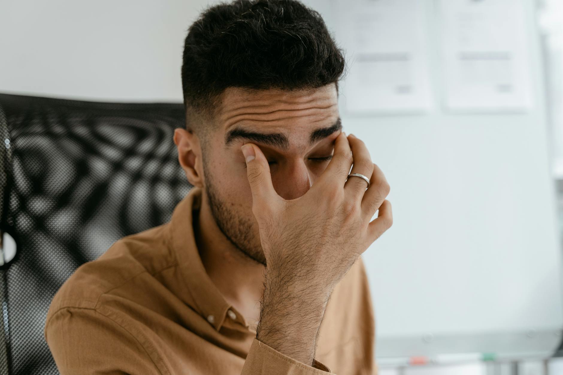 A tired man pressing his eyelids — the unexplained fatigue of evil-eye affliction