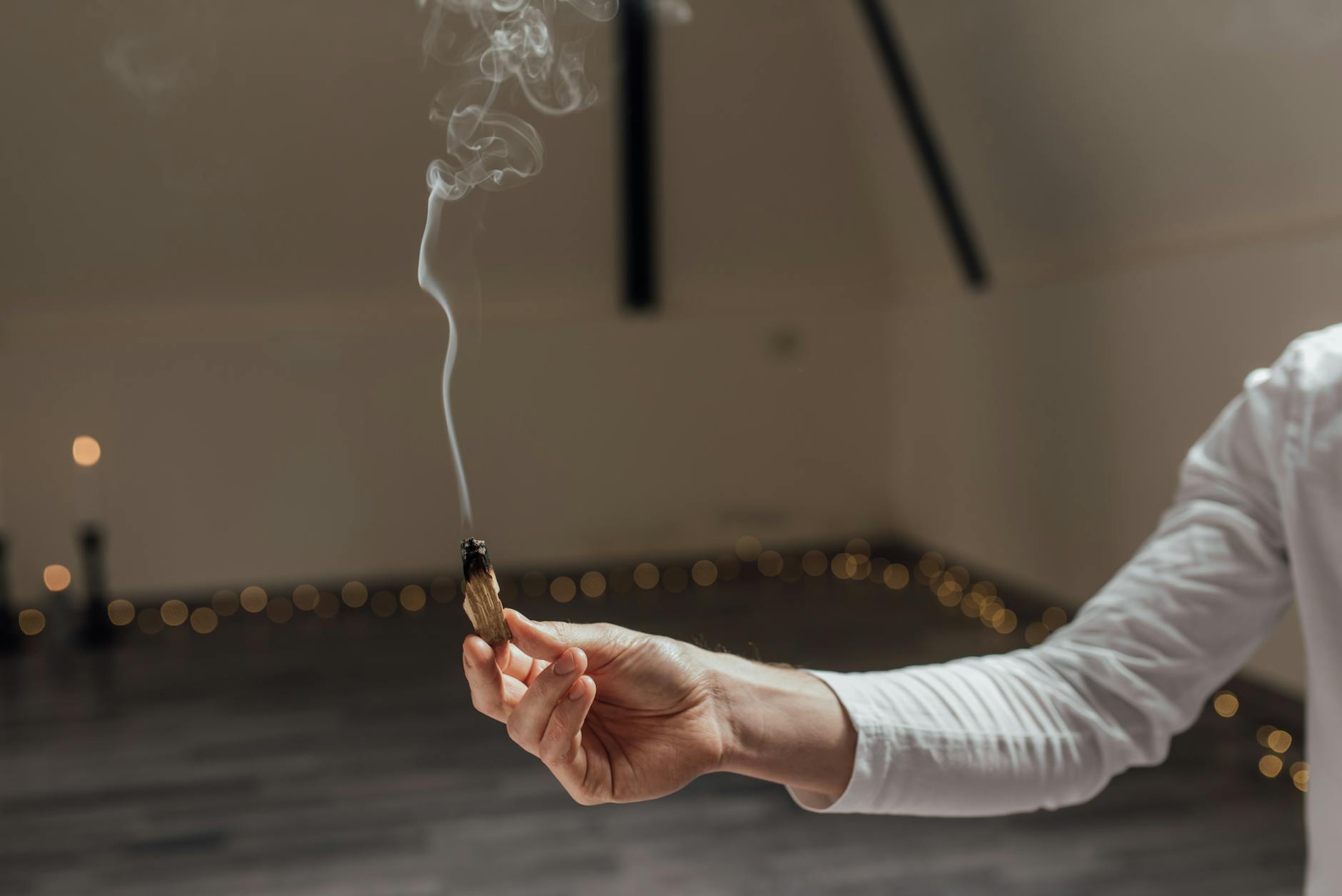 A hand holding a smoking stick of incense during a spiritual offering