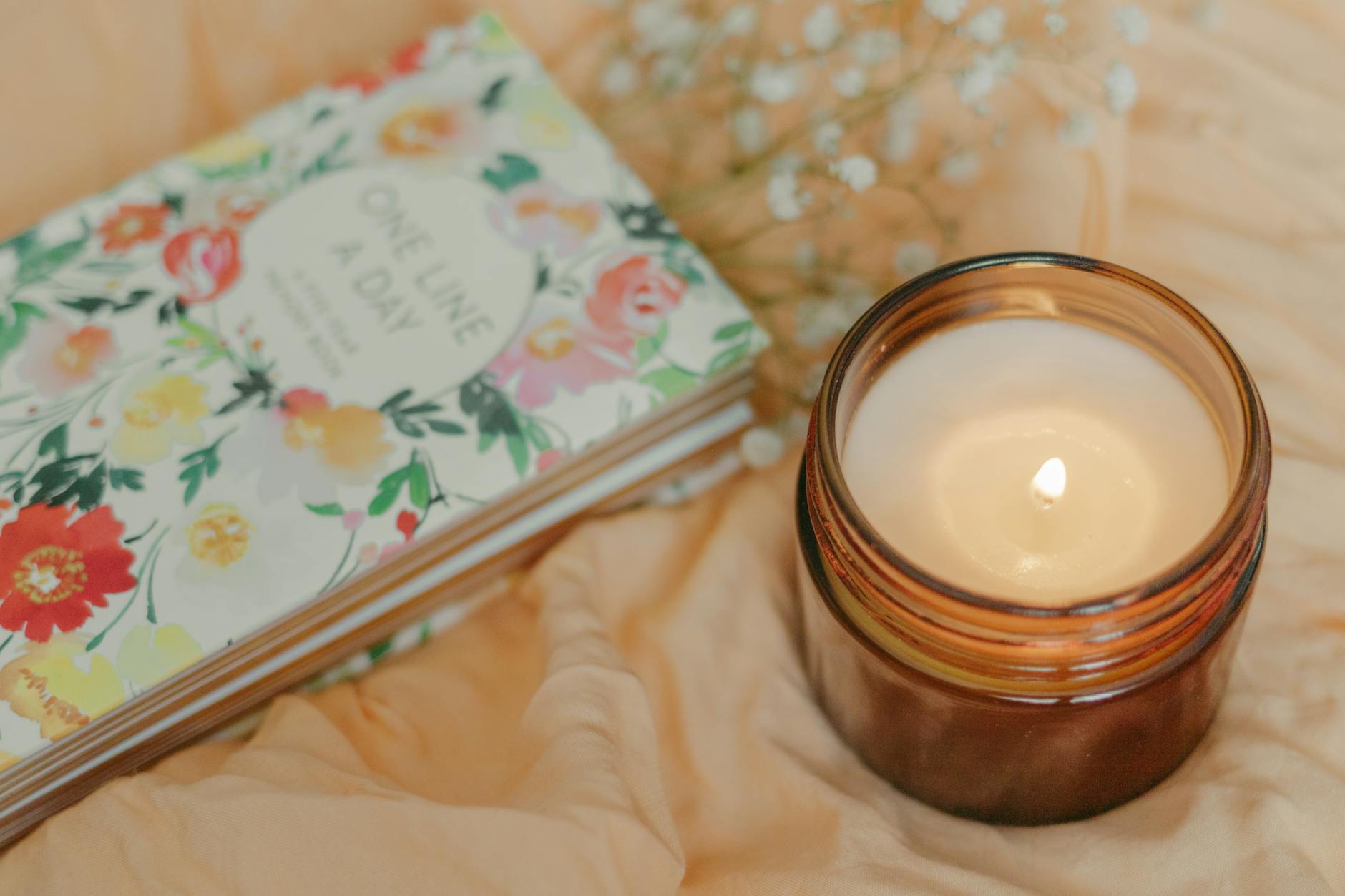 Open journal beside a lit candle in a glass holder, representing writing an intention statement by candlelight