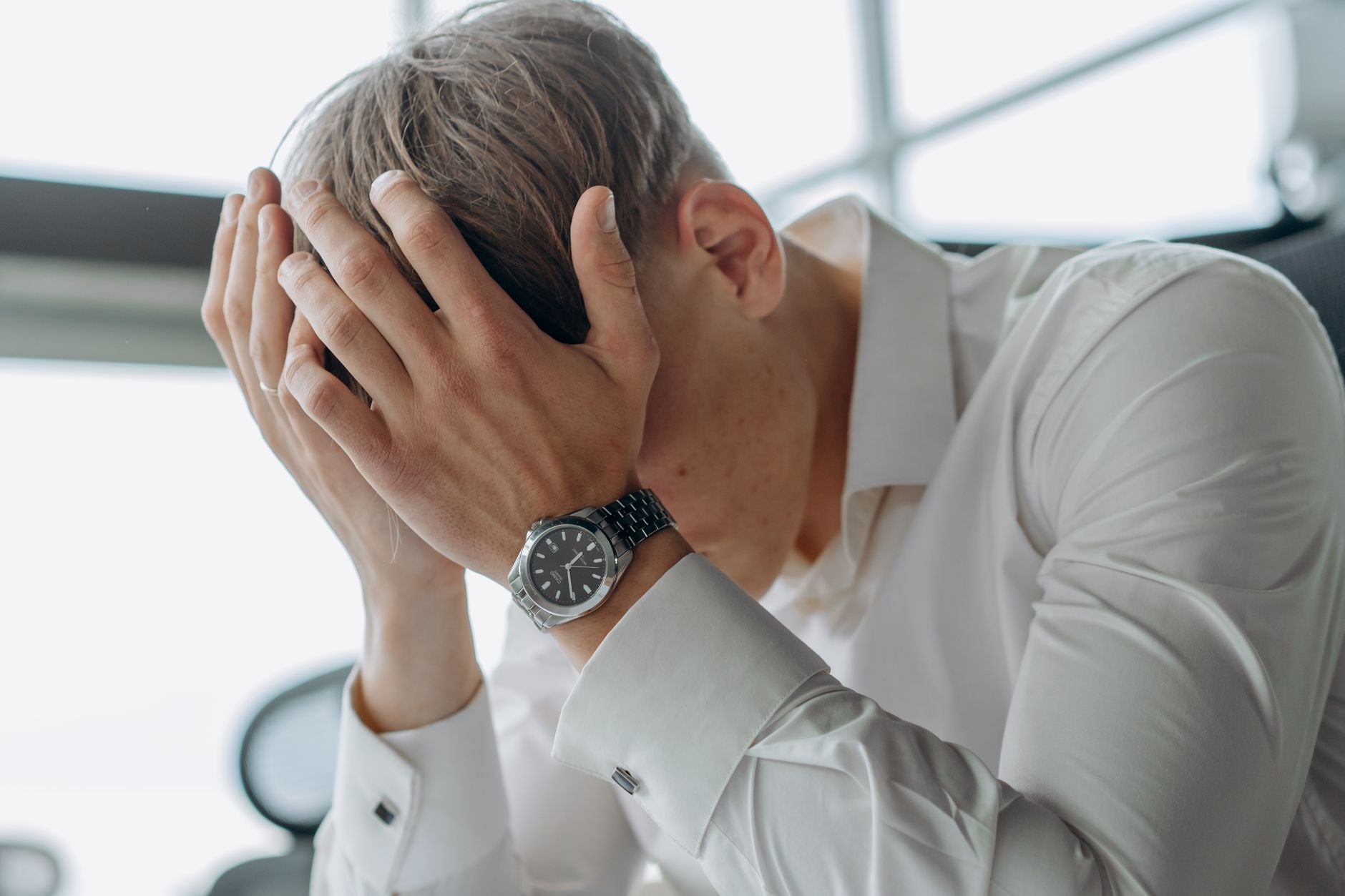 A man sitting with his hands pressed to his head, exhausted and overwhelmed