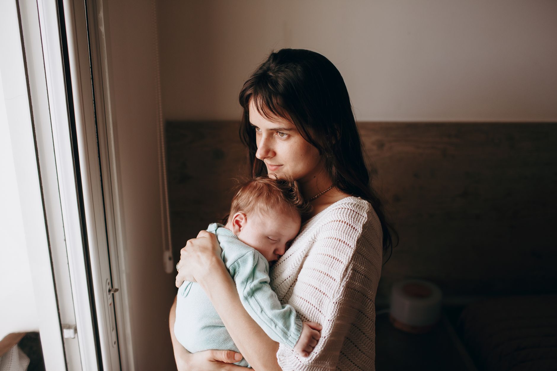 Mother holding child in her arms in soft natural light — the parent field as primary protection