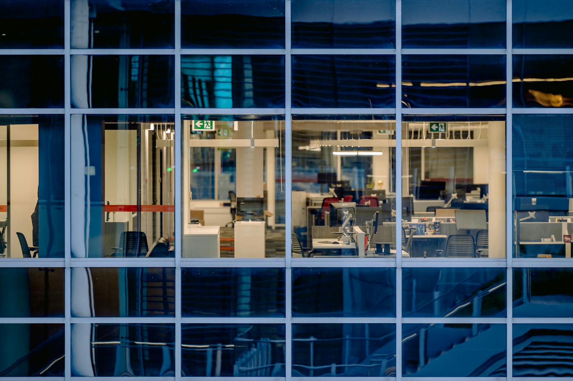 An office tower seen through glass at dusk, desks lit and empty